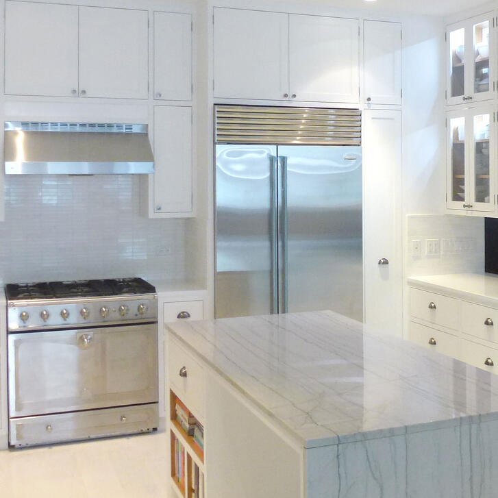 An all white kitchen with a marble counter and cabinetry.