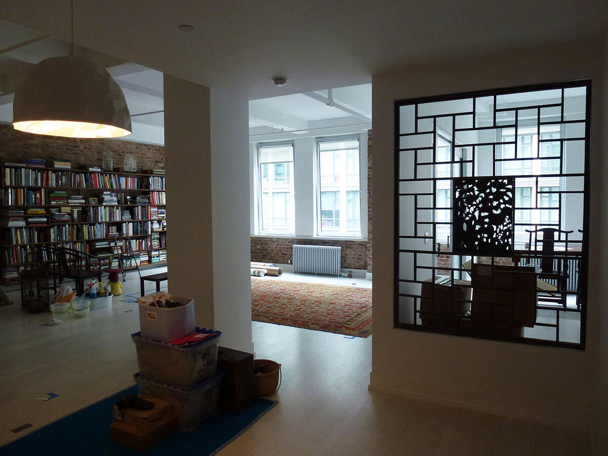 A room with a bookshelf to the far left and windows