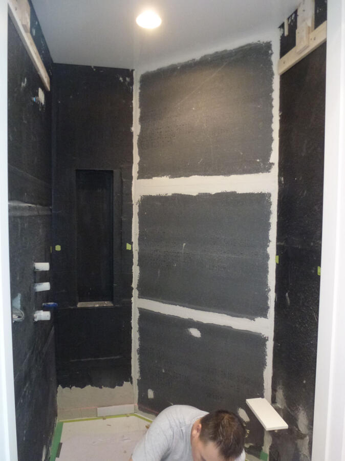 A room with a bookshelf to the far left and windows