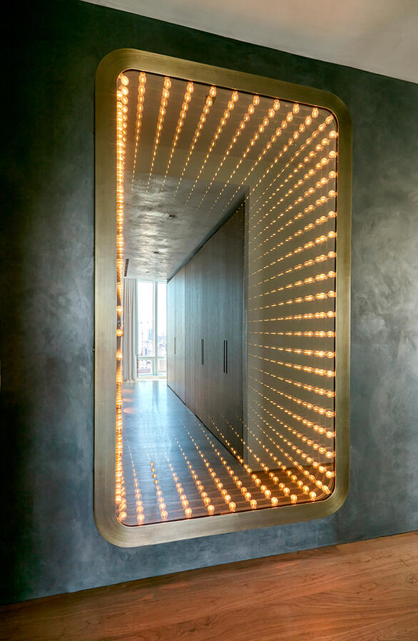 A rounded edged mirror with infinity lights reflecting off of it.