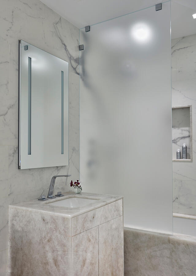 Brightly lit white bathroom with quartz wall and a frosted glass divider